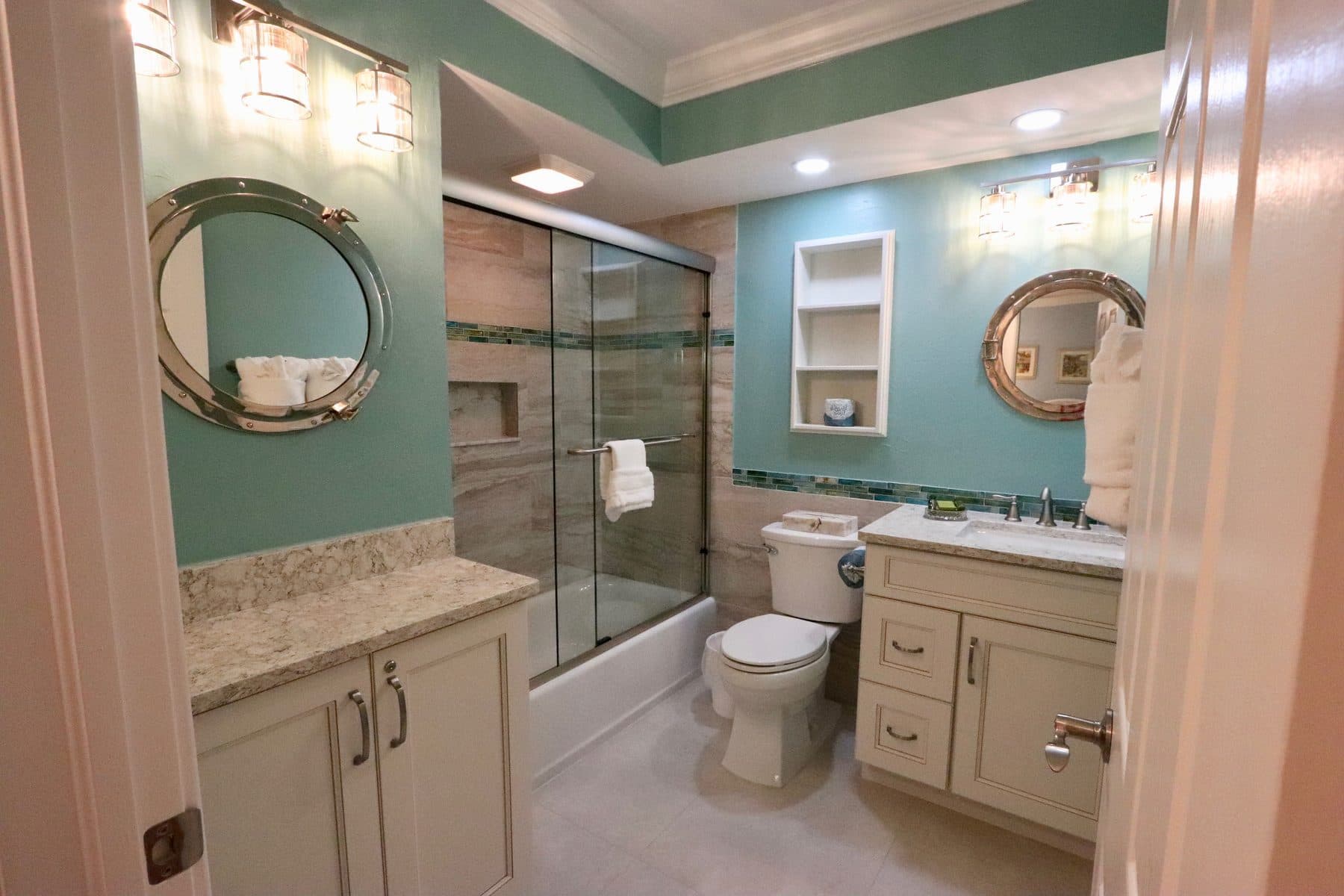 Finished bathroom with teal walls and porthole mirrors